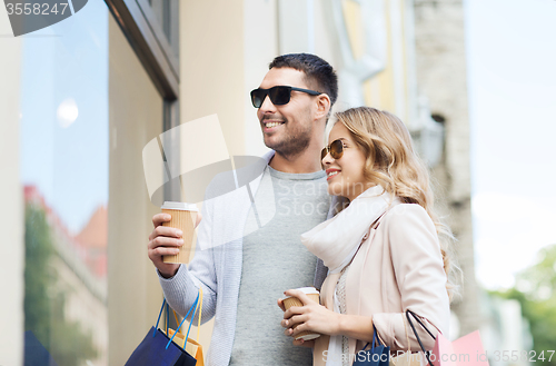 Image of happy couple with shopping bags and coffee in city