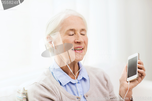 Image of senior woman with smartphone and earphones at home