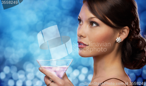 Image of smiling woman holding cocktail over blue lights