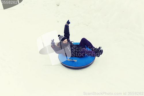 Image of happy young man sliding down on snow tube