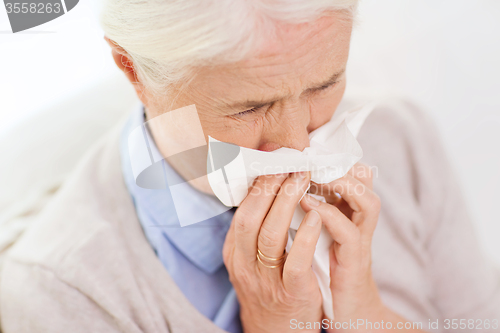 Image of sick senior woman blowing nose to paper napkin