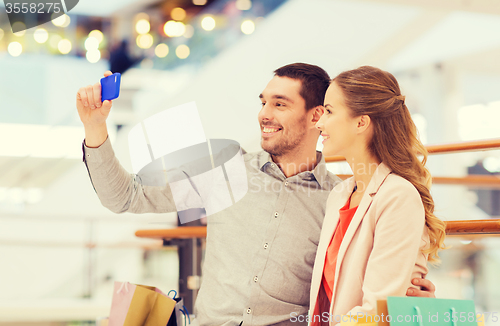 Image of happy couple with smartphone taking selfie in mall