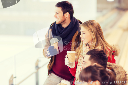 Image of happy friends with coffee cups on skating rink