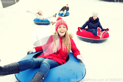 Image of group of happy friends sliding down on snow tubes