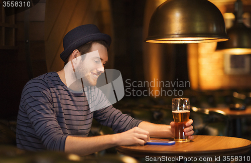 Image of man with smartphone and beer texting at bar