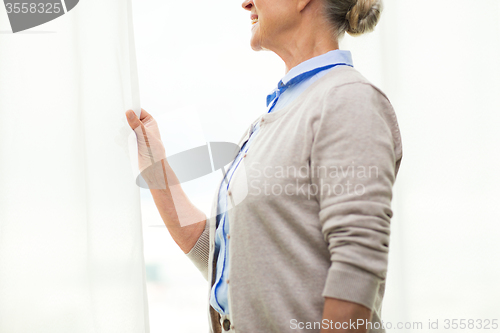 Image of happy senior woman looking through window at home