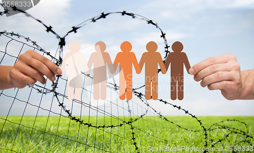 Image of hands holding people pictogram over barb wire