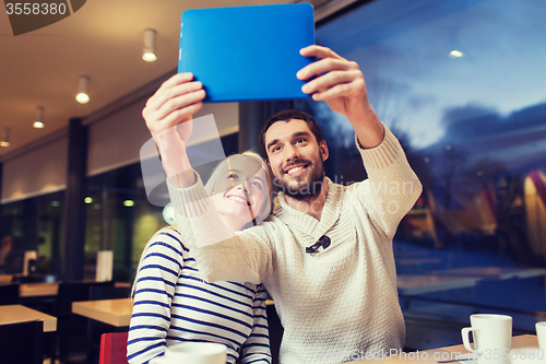 Image of happy couple with tablet pc taking selfie at cafe