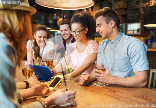 Image of happy friends with tablet pc and drinks at bar