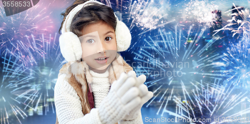 Image of happy little girl wearing earmuffs over firework