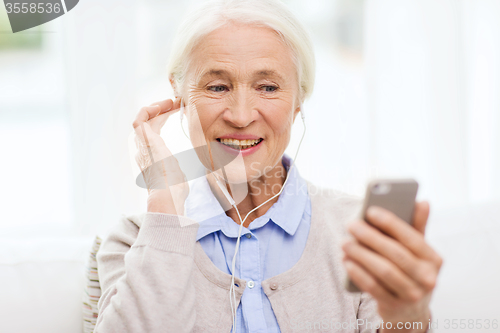 Image of senior woman with smartphone and earphones at home