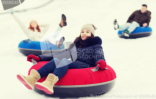 Image of group of happy friends sliding down on snow tubes