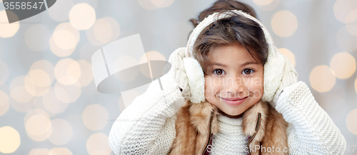 Image of happy little girl in earmuffs over holidays lights