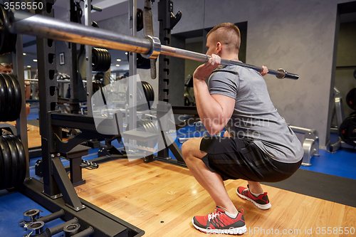 Image of young man flexing muscles with bar in gym