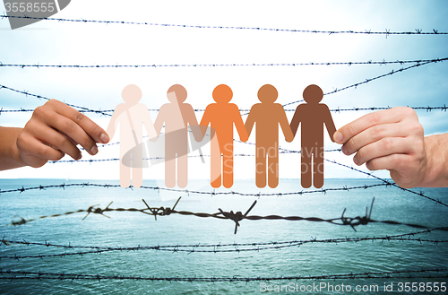 Image of hands holding people pictogram over barb wire