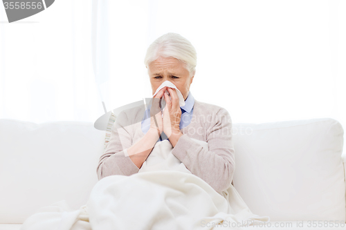 Image of sick senior woman blowing nose to paper napkin