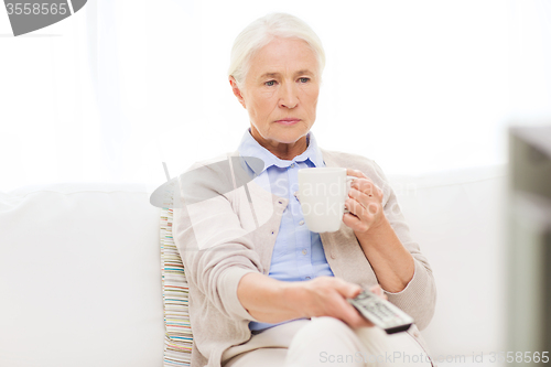 Image of senior woman watching tv and drinking tea at home