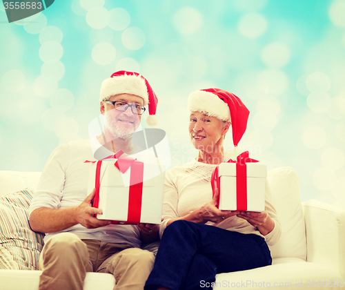 Image of happy senior couple in santa hats with gift boxes