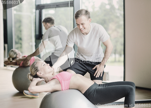 Image of smiling young woman with personal trainer in gym