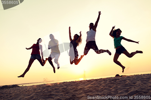Image of smiling friends dancing and jumping on beach