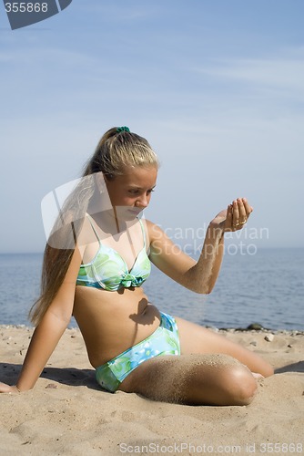 Image of The girl plays with sand on a beach