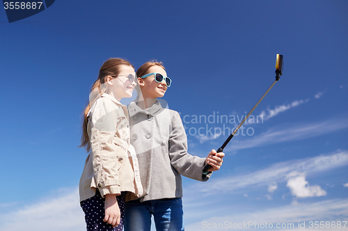 Image of happy girls with smartphone selfie stick