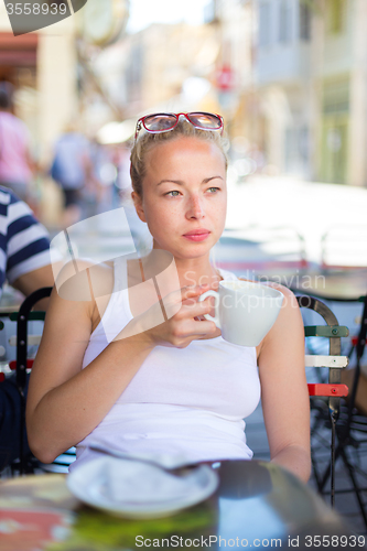 Image of Woman drinking coffee outdoor on street.