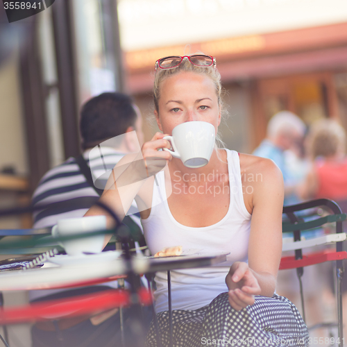 Image of Woman drinking coffee outdoor on street.