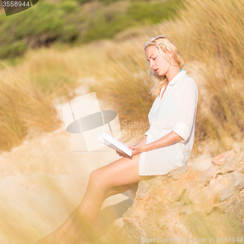 Image of Woman enjoys reading on beautiful sandy beach.