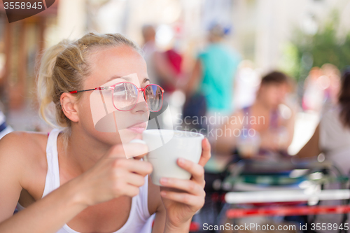 Image of Woman drinking coffee outdoor on street.