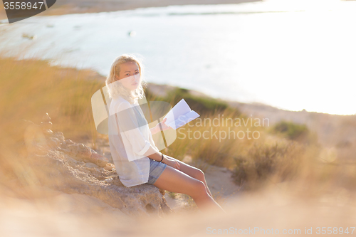 Image of Woman enjoys reading on beautiful sandy beach.