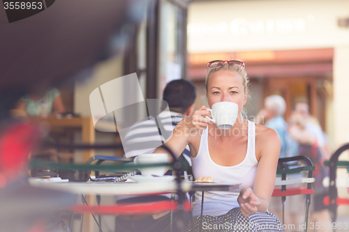 Image of Woman drinking coffee outdoor on street.