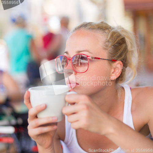 Image of Woman drinking coffee outdoor on street.