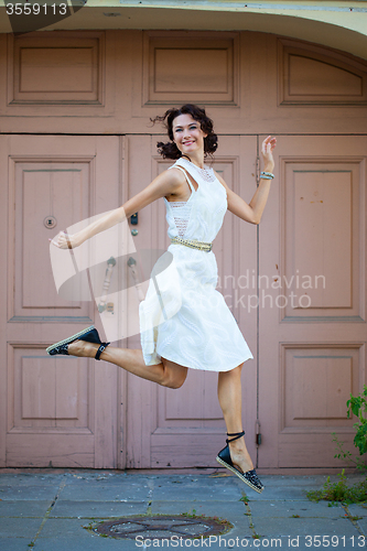 Image of woman in a white dress smiles and jumps near the old door