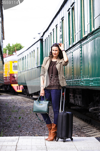 Image of pretty woman with a suitcase and handbag standing near retro rai