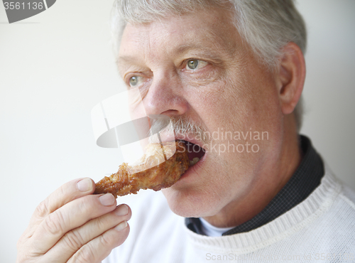 Image of senior man eating fried chicken leg 