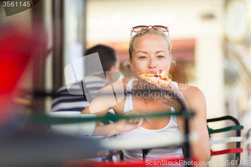 Image of Woman eating pizza outdoor in cafeteria.