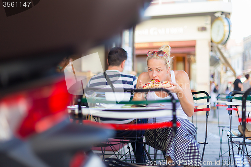 Image of Woman eating pizza outdoor in cafeteria.