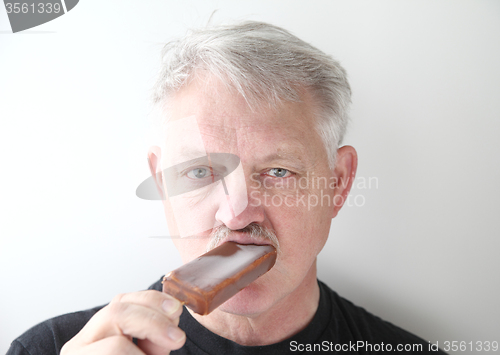 Image of Man eats chocolate ice cream bar. 
