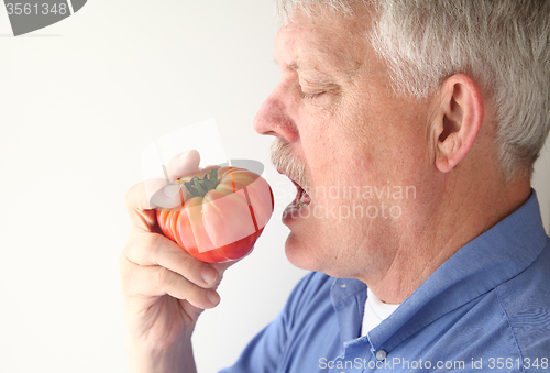 Image of Senior man eating big tomato