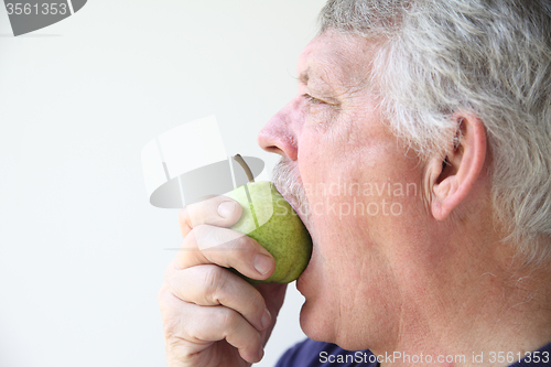 Image of Older man bites into pear. 