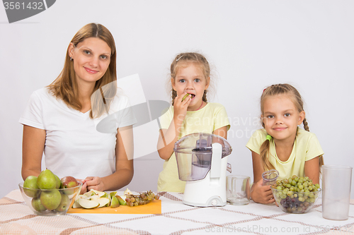 Image of Mom and daughter sit at the table with a juicer and fruit