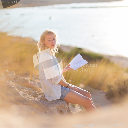 Image of Woman enjoys reading on beautiful sandy beach.