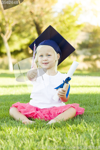 Image of Little Girl In Grass Wearing Graduation Cap Holding Diploma With