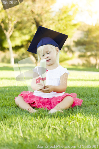 Image of Little Girl In Grass Wearing Graduation Cap Holding Diploma With