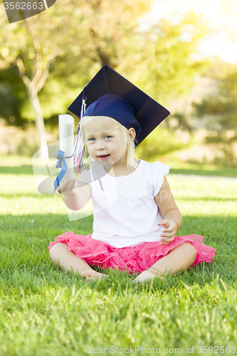 Image of Little Girl In Grass Wearing Graduation Cap Holding Diploma With