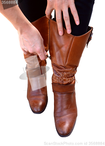 Image of Woman holds her brown leather boots while zipping them up