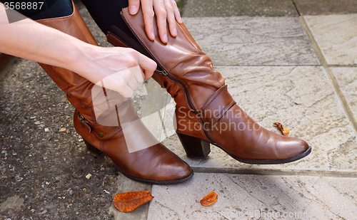 Image of Woman zipping up high-heeled tan leather boots