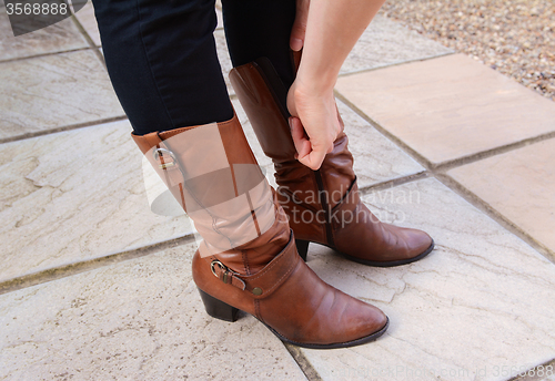 Image of Young woman zipping up her fashionable leather boots