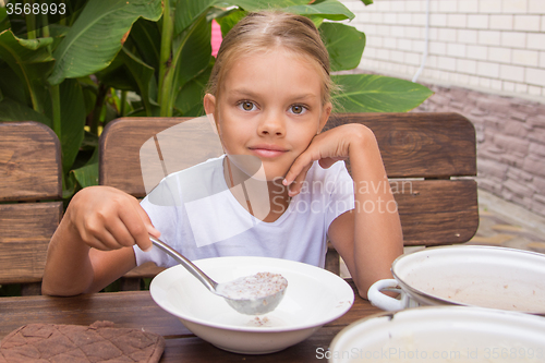 Image of Girl with a ladle in the bowl puts porridge for breakfast